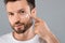 Closeup of bearded man applying face cream on grey