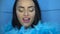 Closeup of beautiful brunette woman smiling and looking into the camera with blue feather boa over blue wall background