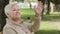 Closeup beautiful elegant elderly woman sitting on bench in city park waving hand welcoming friend. Adult mature smiling