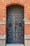 Closeup of an beautiful old black rustic wooden door entrance on a brick building. Ornate decorative iron fittings.