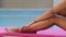 Closeup beautiful slender tanned girl feet on pool background. Young shapely woman with bottle of sunscreen lotion