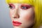 Closeup beauty portrait of calm cute young female model with freckles, red makeup and yellow wig, looking forward with serious