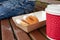 Closeup of beignet pastries, donuts in a paper takeaway box and a cup of coffee on a bench in park. The delicious