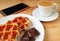 Closeup Belgian Waffles and Dark Chocolate Chunks with Blurry Hot Coffee and Smartphone in Background