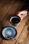Closeup black americano coffee in blue cup in male hand, saucer with vintage tea spoon on wooden brown vintage