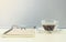 Closeup black coffee in transparent cup of coffee brown note book with glasses on blurred wooden desk and frosted glass wall textu
