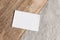 Closeup of blank business card on teak wooden table. Blurred beige linen background. Empty paper card mockup scene in