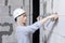 Closeup blonde girl designer foreman in white construction helmet measures the grey wall of sibit by tape measure in house under