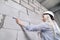 Closeup blonde girl designer foreman in white construction helmet measures the grey wall of sibit by tape measure in house under