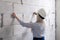 Closeup blonde girl designer foreman in white construction helmet measures the grey wall of sibit by tape measure in house under