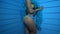 Closeup body of beautiful seductive woman dancing wearing yellow bikini and blue feather boa over blue wall background