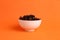 Closeup of a bowl full of raisins on an orange surface
