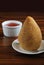 Closeup of brazilian snack called Coxinha with portion of catchup in the background. Brazilian food