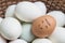 Closeup brown chicken egg with paint in smile face on pile of white duck egg on wood basket background
