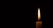 Closeup burning single candle flame isolated on black background with copy space