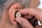 Closeup Of Businessman Inserting Hearing Aid In Ear