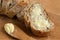 Closeup of buttered slice of whole wheat rustic bread next to cut bread and wood knife. Light wood board