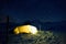 Closeup of a camping tent is situated in the snow, illuminated by the starry night sky