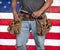 Closeup carpenter holding hammer and wearing worn out old, leather tool belt with hand tools in front of American flag