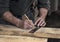 Closeup of carpenter`s rough rugged hands using a pencil and old square to mark a line on wood board to cut