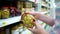 Closeup caucasian woman hands near shop shelves choosing marinade green olives in grocery market