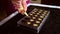 Closeup of chef pastry chocolatier pouring liquid creamy filling into chocolate molds to preparing delicious handmade pralines at