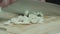 Closeup of the chefâ€™s hands finely chopping garlic with kitchen knife on a wooden cutting board.