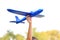 Closeup child hand raise up a blue toy airplane flying over white sky background in the garden