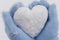 Closeup cozy female hands in blue fluffy mitten with heart of snow in winter day. Love concept. Snow falls. Valentine day