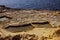 Closeup of a cracked Malta beach view with checkerboard-like salt pans, sunlit seascape background