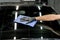 Closeup cropped image of hand of young man worker of auto service, wiping and polishing the windscreen of modern black