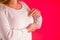 Closeup cropped portrait young woman with breast pain touching chest, on pink background