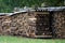 Closeup of cut wooden planks stacked on each other under a metallic roof near the field