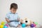 Closeup cute asian kid look at the tablet at home on gray carpet with doll and colorful ball and cement wall textured background w