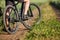 Closeup of cyclist man legs with mountain bike on outdoor trail in the summer field.