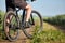 Closeup of cyclist man legs with mountain bike on outdoor trail in the summer field.