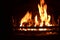 Closeup of dancing flames of burning wooden logs in fireplace with black background warming light in Christmas holidays.