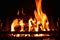 Closeup of dancing flames of burning wooden logs in fireplace with black background warming light in Christmas holidays.