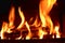 Closeup of dancing flames of burning wooden logs in fireplace with black background warming light in Christmas holidays.