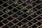 Closeup of a diamond-patterned wire mesh with plants behind it