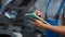 Closeup digital tablet in male hands at background of open car hood in garage. Unrecognizable Caucasian auto mechanic