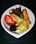 Closeup of a display of assorted sliced fruits on a white plate with a black background