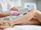 Closeup. Doctor-cosmetician in gloves performes a procedure on patient leg with medical equipment laser in equiped beauty shop