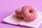 Closeup of donuts covered with pink icing and colored pastry topping on a pink background.