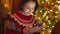 closeup dreamy smiling woman in cute red festive sweater on background of lights using phone, texting, messaging