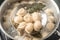 Closeup of dumplings on skimmer over stewpan with boiling water.