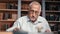 Closeup elderly gray haired man reading book working at library desk searching historical research