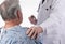 Closeup of a elderly male patient wearing a hospital gown as a doctor places his hand on his shoulder offering comfort