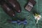 Closeup of elegant stylish dark male accessories on green background. Top view of bow-tie, shoes, floral corsage, golden