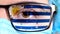 Closeup, eye, part of doctor face in medical mask, glasses, which painted in colors of Uruguay flag. Many viruses, germs